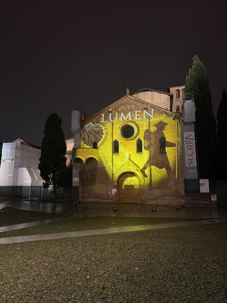 Historic brick church illuminated with golden light projection displaying "LUCE LUMEN" text at night