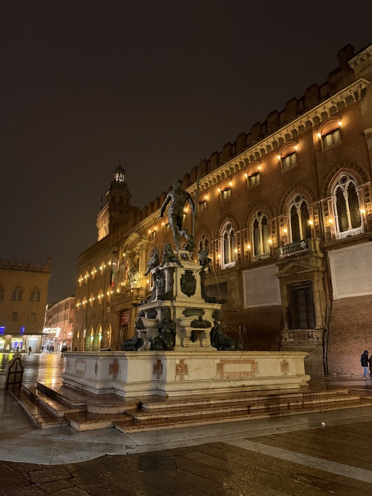 Night view of illuminated medieval buildings and bronze statue monument in historic Italian piazza