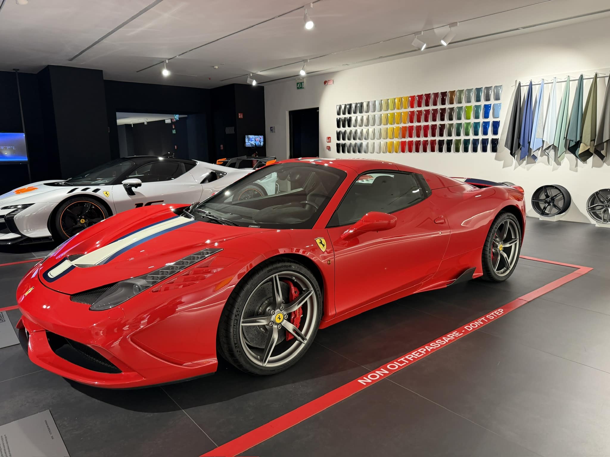 A stunning red Ferrari with racing stripes sits prominently in a sleek automotive showroom