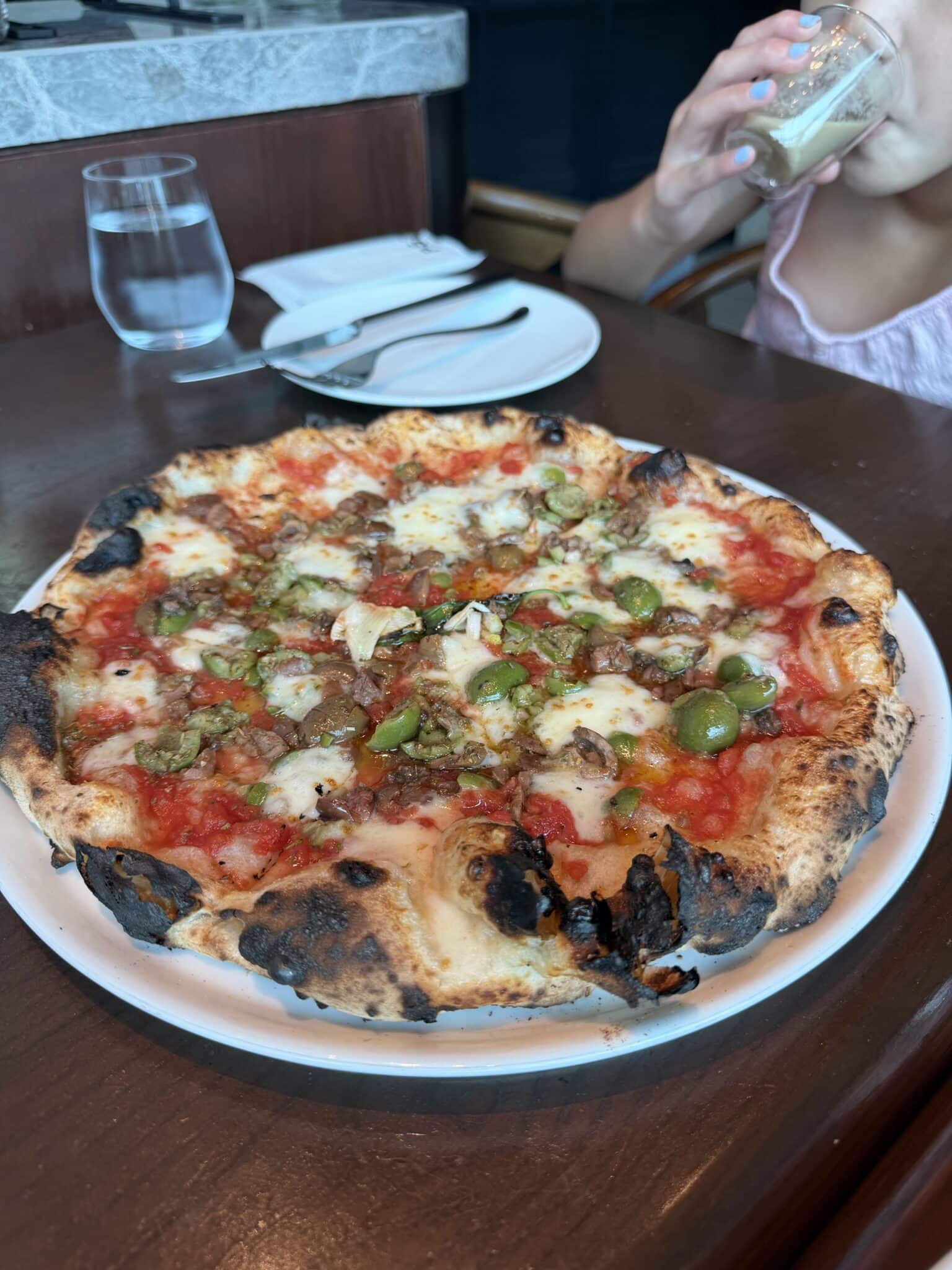 Wood fired pizza with green olives and a charred blistered crust in Naples