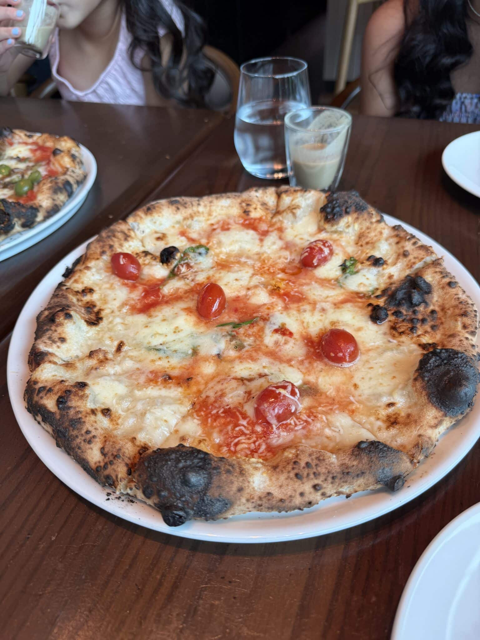 Wood fired margherita pizza with blistered crust and fresh cherry tomatoes fresh from the oven
